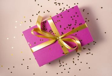 Pink Gift box with yellow ribbon and sprinkled yellow heart glitters with light pink background - Personalized Gifts